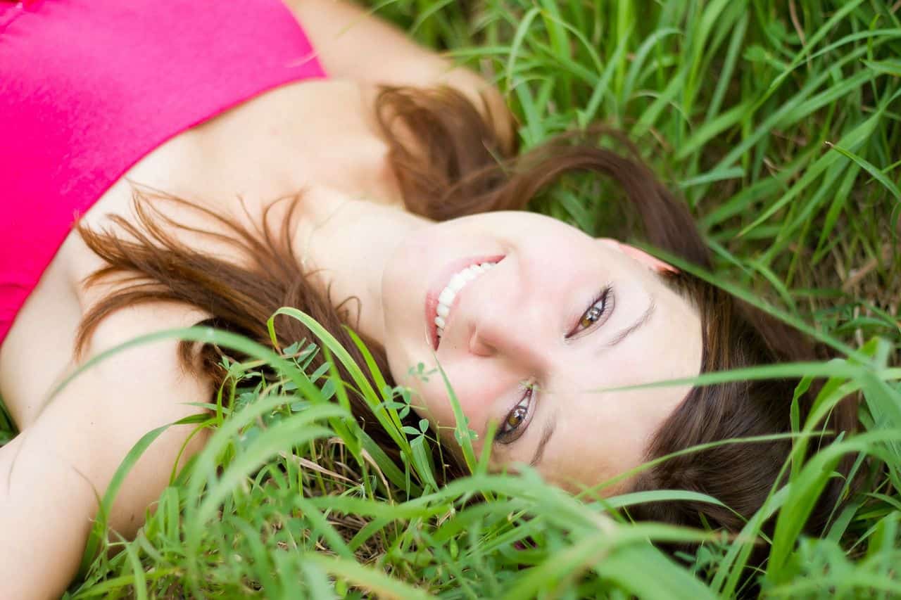 Eine verzaubernde Frau liegt fröhlich mit einem Lachen im grünen Gras