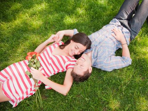Mann und Frau liegen gemeinsam im Gras und lachen sich verführerisch an